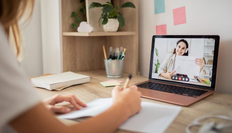Mulher escrevendo em caderno durante aula online