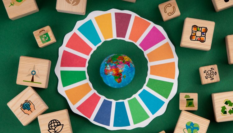 Peças em formato de cubo de madeira com as imagens de cada ODS, no centro da imagem uma cartela de cores redonda com um mini globo terrestre no meio